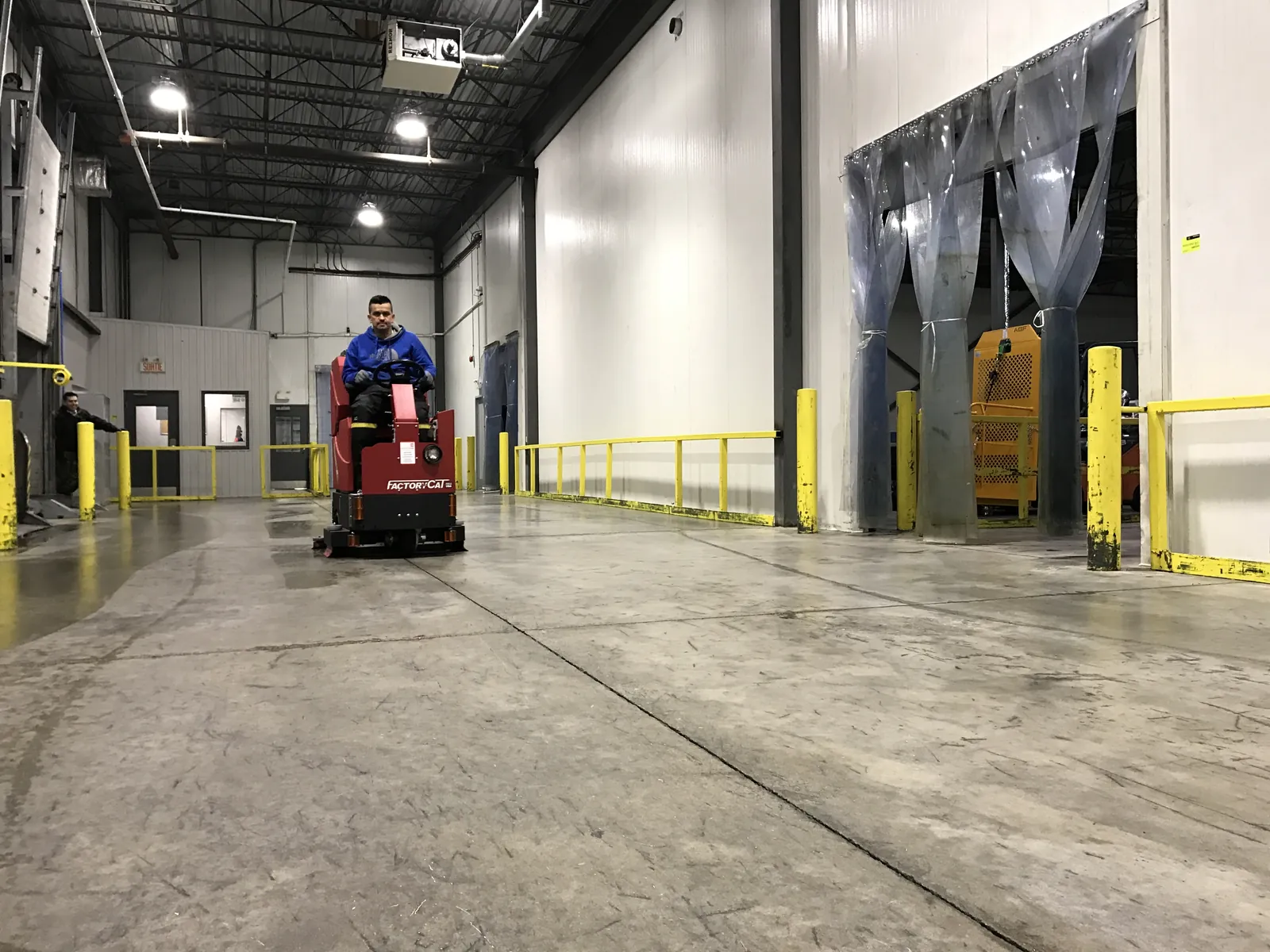 An operator using a ride-on floor-cleaning machine in an industrial space.
