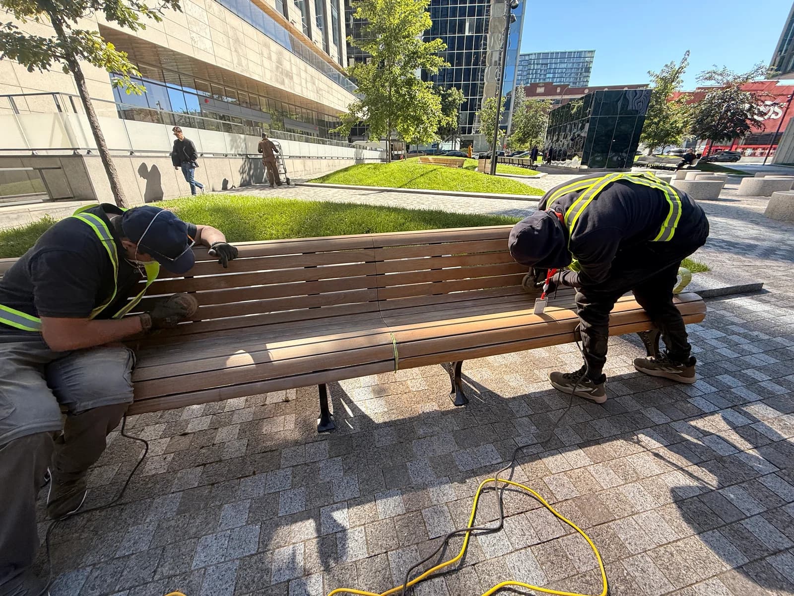 Deux membres de l’équipe poncent les lattes d’un banc extérieur en bois.