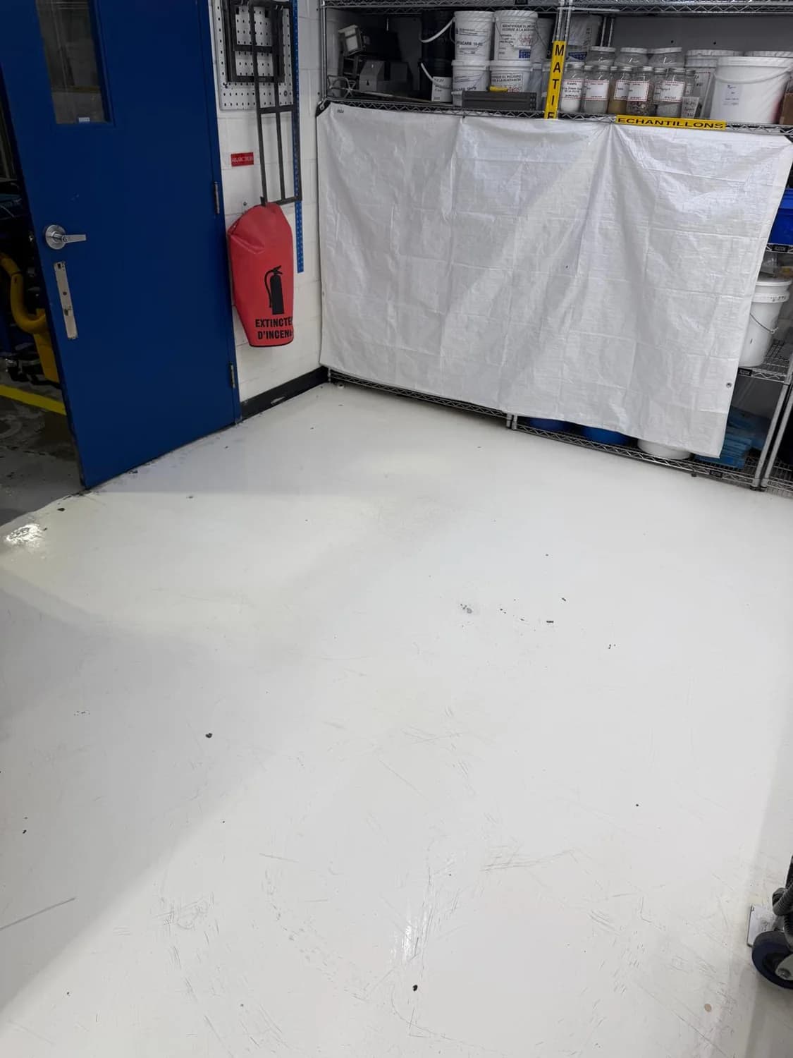 Oldcastle laboratory floor beside a blue door and storage shelving.