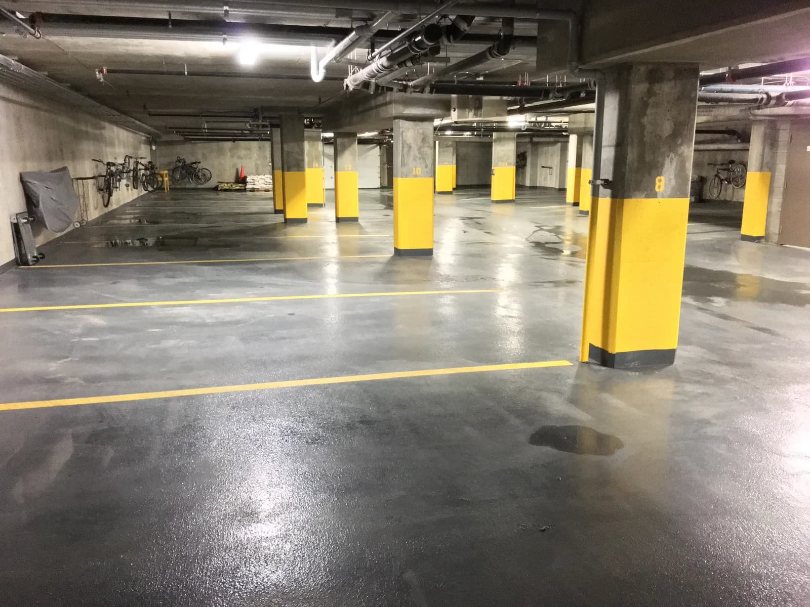 Surface de béton et colonnes jaunes dans un stationnement intérieur après une intervention de nettoyage.
