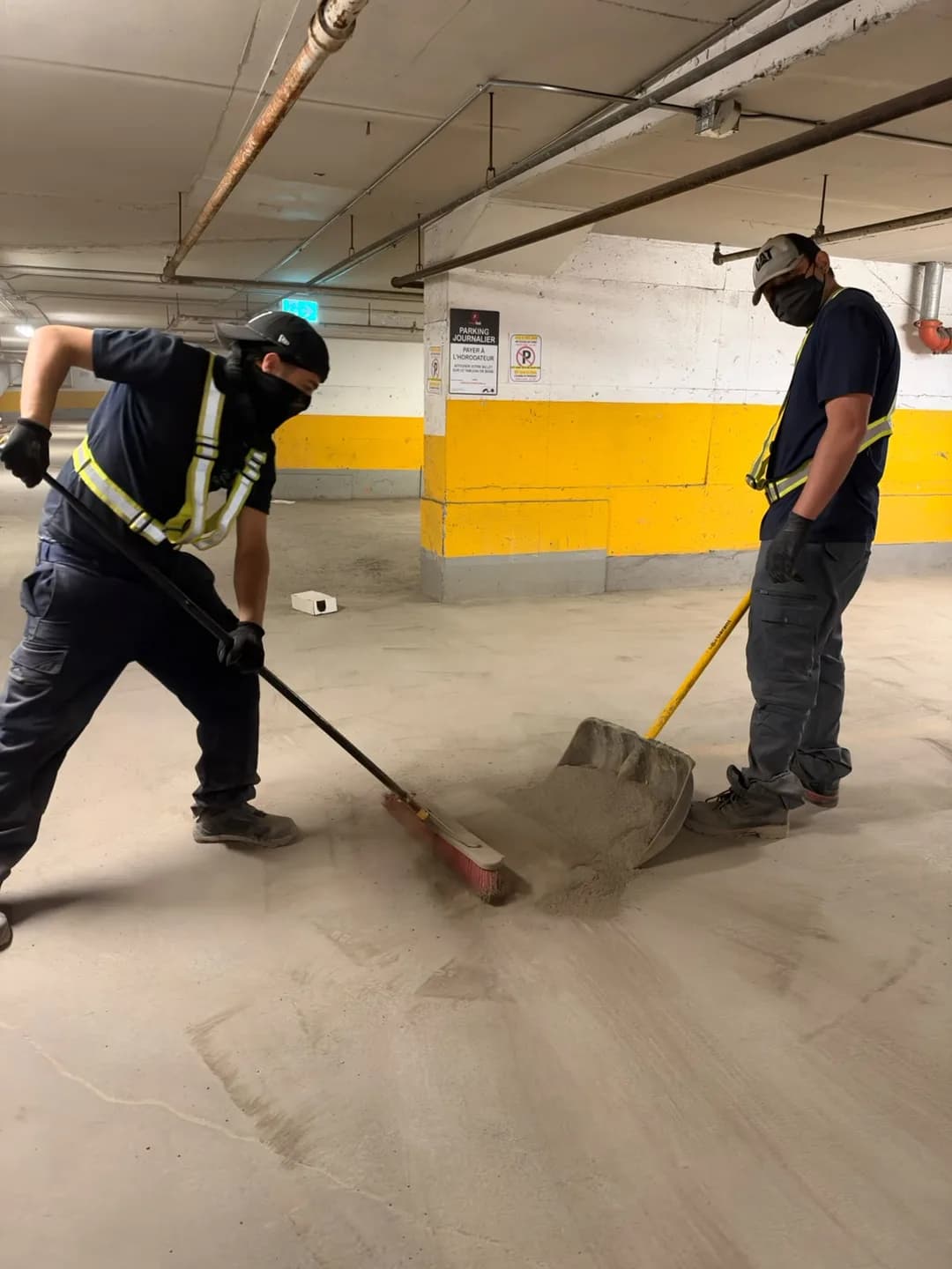 Two Push Push team members collect debris with a broom and shovel in the CAPREIT parking garage.